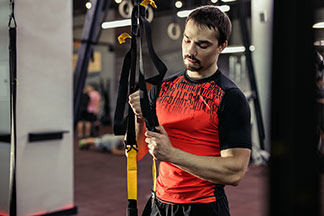 Renkli bir spor tişört giymiş sportif bir erkek, spor salonundaki bir spor ekipmanını ayarlıyor.