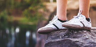 Sportif erkek çorapları: Bir kayanın üzerinde dururken beyaz sneaker ayakkabılar ve siyah sneaker çorapları giyen genç bir erkeğin bacaklarının yakından görünümü.
