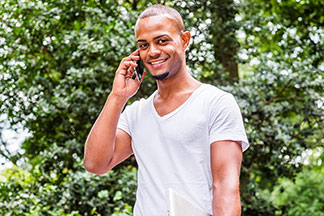 Beyaz, V yakalı bir tişört giyen genç bir erkek parkta telefonla konuşuyor.