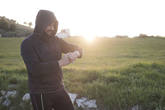 Spor için sweatshirt'ler: Siyah kapüşonlu bir sweatshirt ayrıca eşofman giymiş bir erkek dışarıda duruyor, kapüşonunu yukarı çekiyor ve saatine bakıyor.